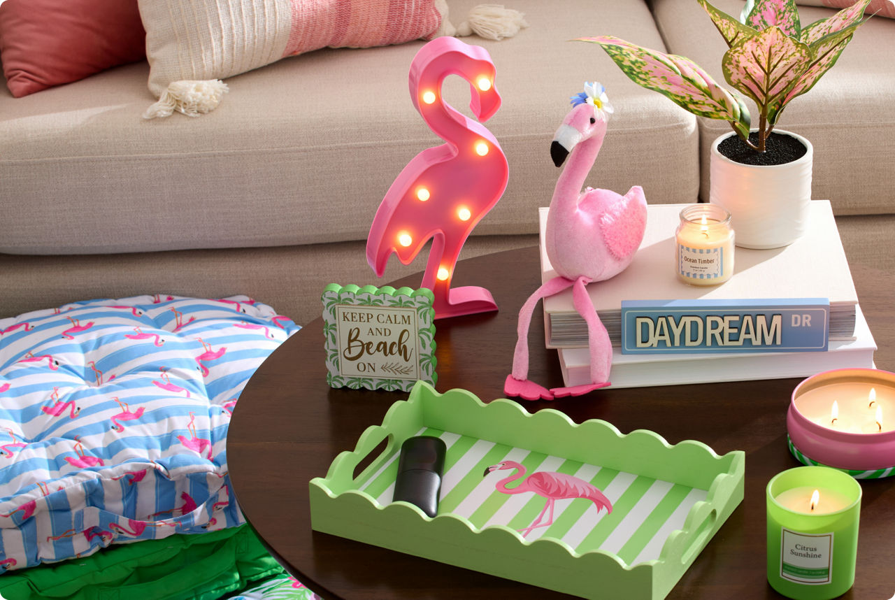 Flamingo-themed home décor grouping with light‑up pink flamingo figurines, tropical accent tray, scented candles, throw pillows, and decorative coffee table styling for summer or coastal home décor.
