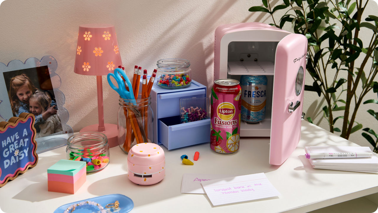 Pastel desk organizer with compartments holding push pins, sticky notes, pens and office supplies in soft blue and pink tones
