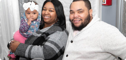 Couple looking at camera and smiling while the mom holds a baby.
