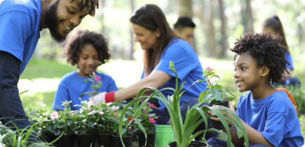 Two adults and two kids smiling while working on planting a flower garden.