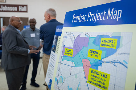 Sign with a map that says Pontiac Project Map with residents talking in the background.