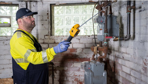 DTE employee wearing uniform and inspecting gas meter in a basement