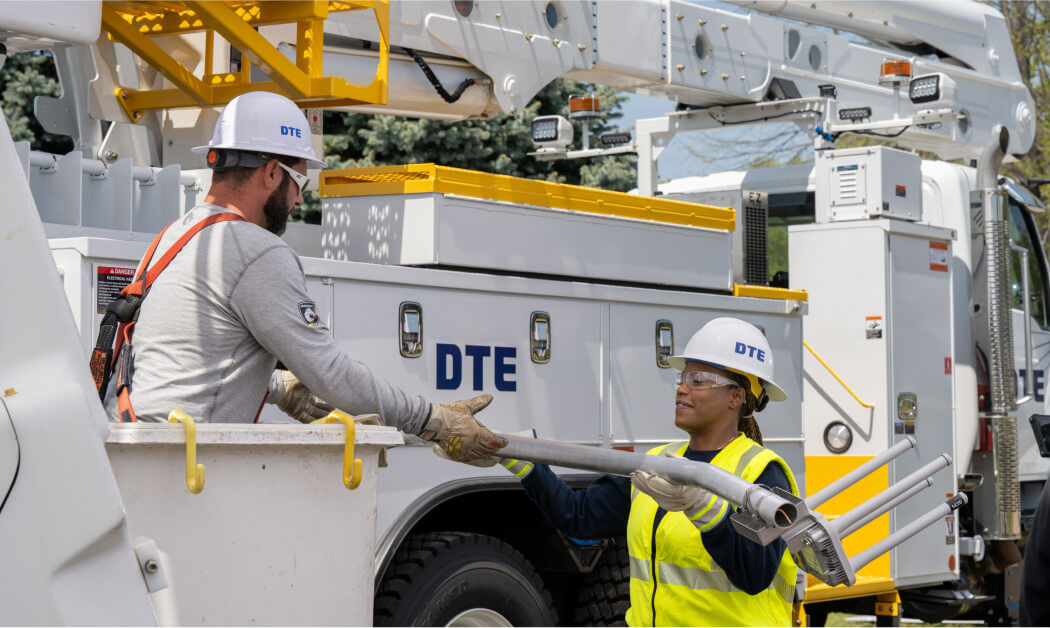 DTE employee in utility bucket truck handing equipment to another employee
