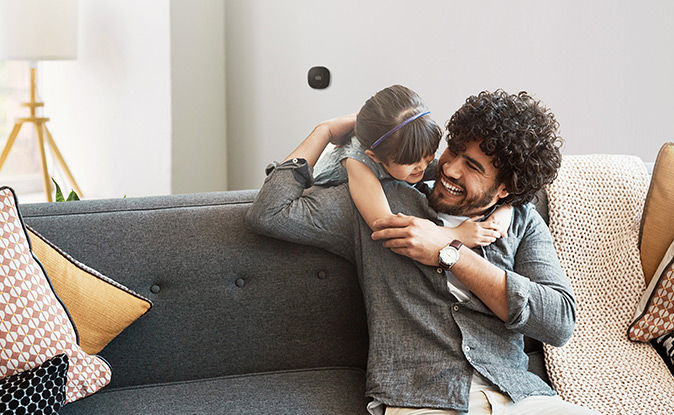 Man with his daughter hugging him and smiling with a smart thermostat in the background