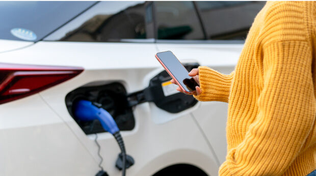 Woman charging electric vehicle and looking at phone
