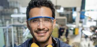 man smiling with protective glasses in a manufacturing setting in the background