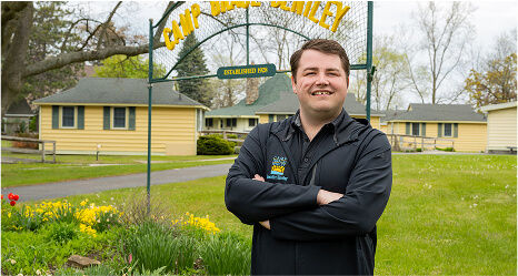 Man smiling at the camera with sign behind Camp Grace Bentley