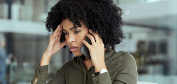 A woman with curly hair holds a phone to her ear, looking stressed, with one hand on her forehead