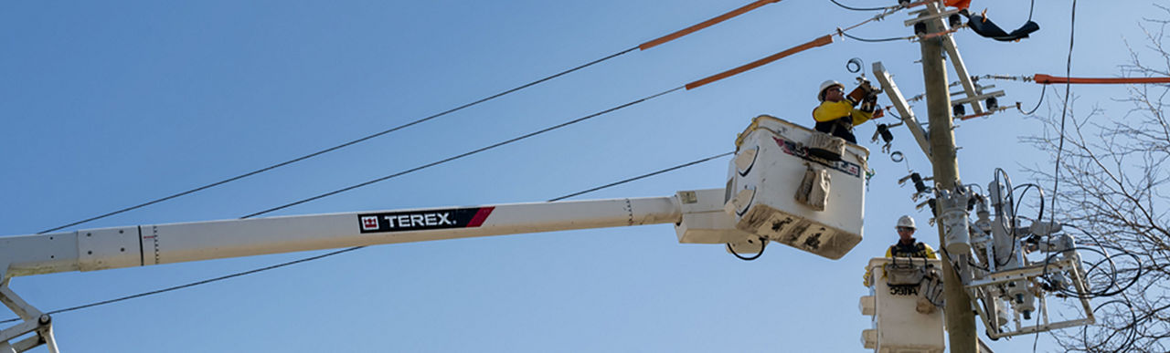 Two DTE linemen working on a recloser installation with blue sky background