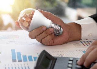 Man holding an energy efficient lightbulb filled with pennies over a paper chart