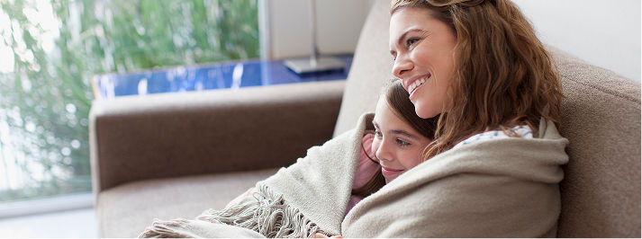 Mom and daughter wrapped in a blanket sitting on a chair. 