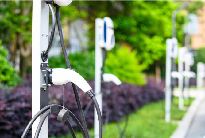 Row of electric vehicle level 2 chargers outdoors with green and purple plants.