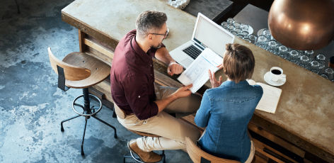 man and woman sitting at a table with a laptop and document discussing their DTE rebates while drinking coffee 