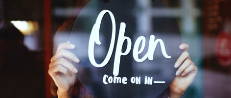 Woman holding open come on in sign on the window of small business serviced by DTE