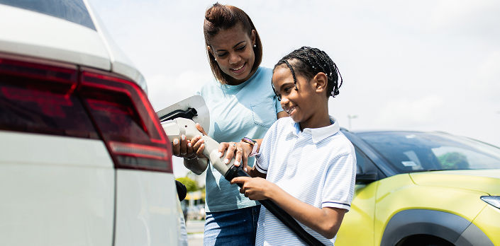 Mother and son charging electric vehicle outdoors on a sunny day.