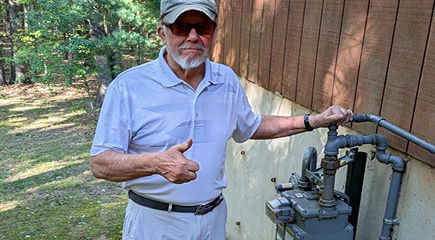 Man looking at camera with thumbs up next to a natural gas meter outside his home.