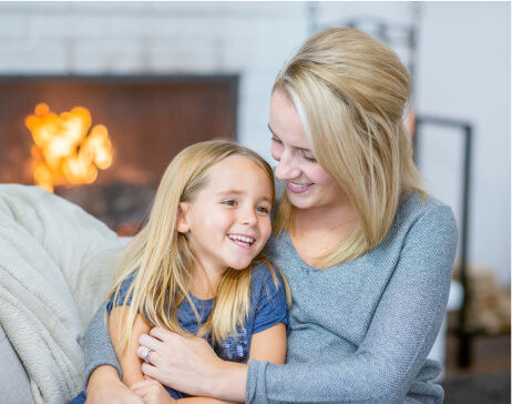 Mom and daughter sitting on a couch and smiling with a fireplace in the background