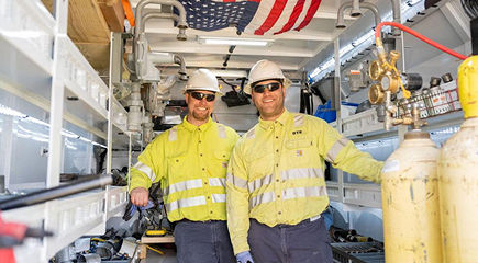 Two DTE employees in yellow safety jackets inside a natural gas service station.