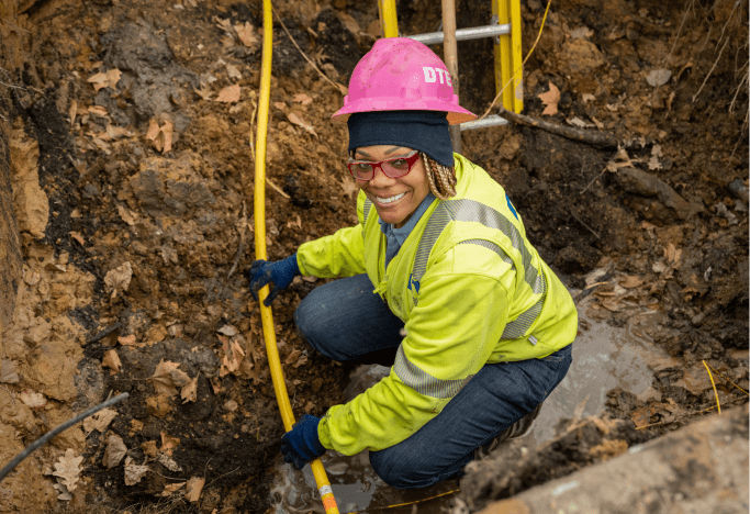 DTE employee wearing pink hard hat and yellow safety vest looking at camera smiling while upgrading gas lines.