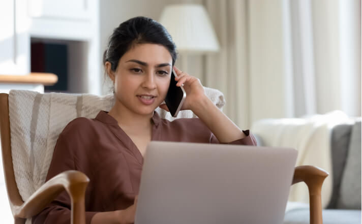 Woman sitting while on a phone call looking at her laptop 