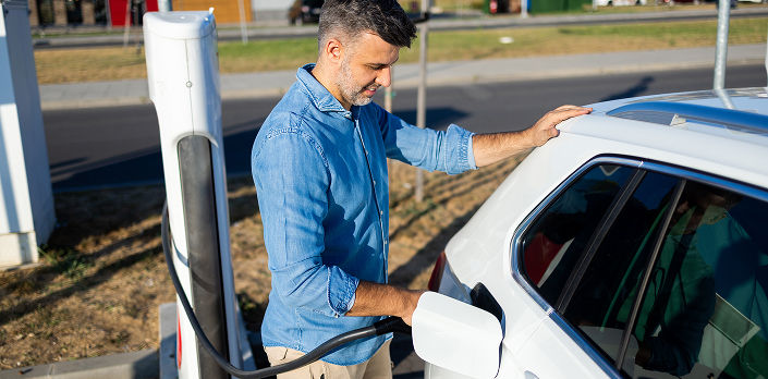 Man in collar shirt charging electric vehicle in a parking lot.
