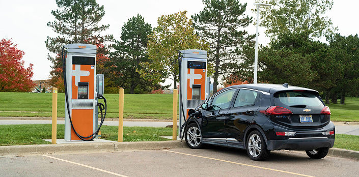 Two DC faster chargers in a parking lot with an EV car.