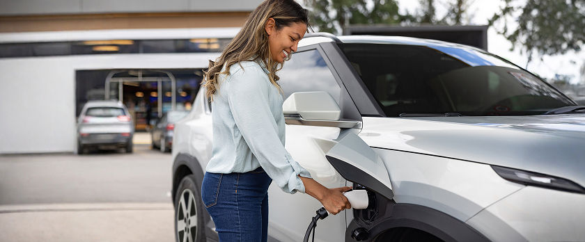 Woman charging her electric vehicle with a Level 2 charger in a parking lot.