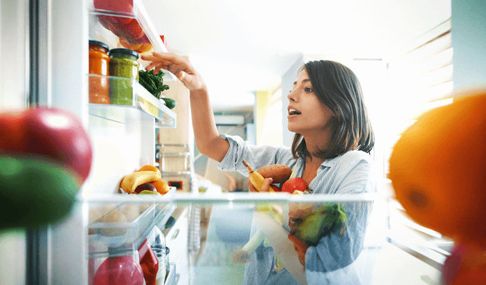 Young girl looking in a fridge while holding produce