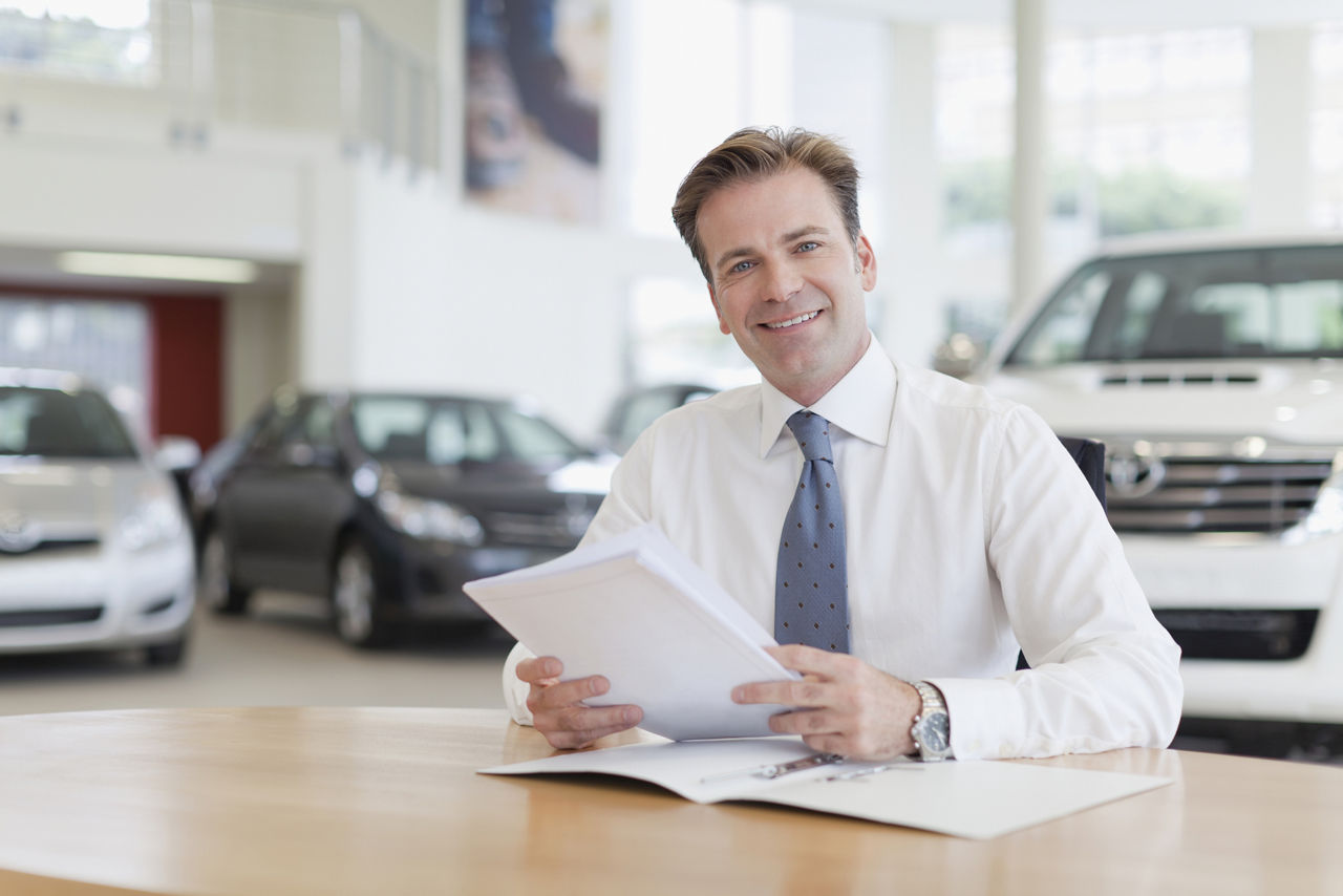 Man in a car dealership smiling holding contract papers