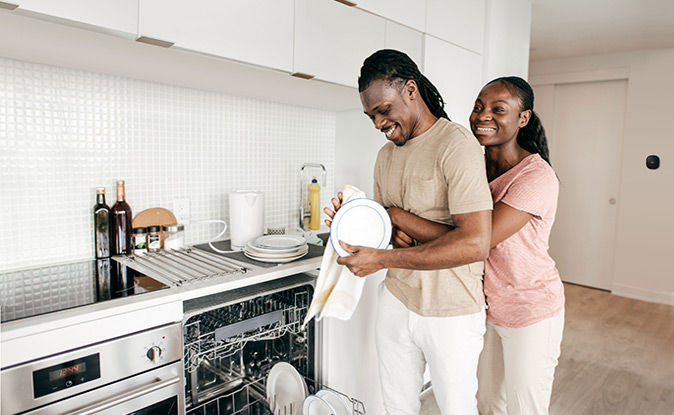 Cuple smiling while drying the dishes and a smart thermostat in the background