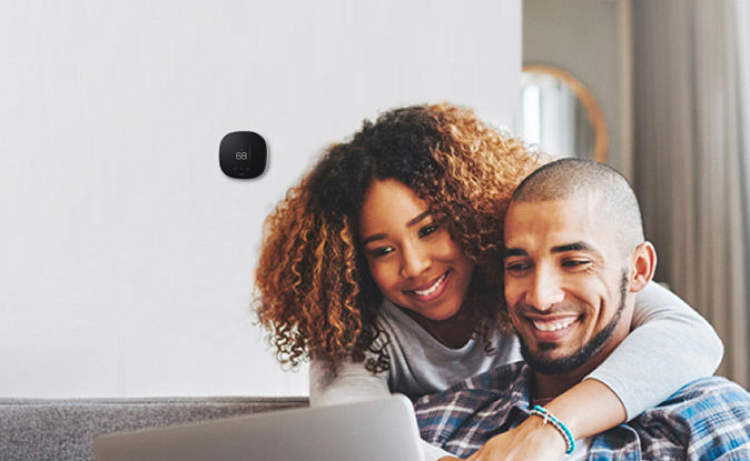 Cuple smiling while drying the dishes and a smart thermostat in the background