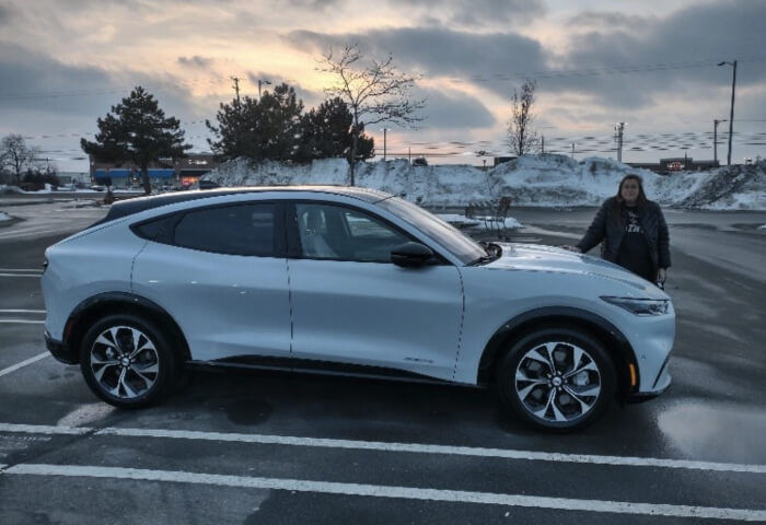 Woman standing behind her white Ford Mach-E