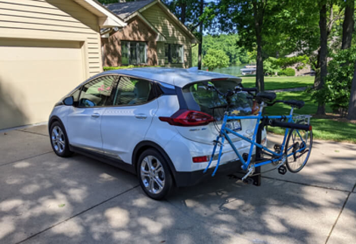 A white Chevy Bolt on a home's driveway with a blue bicycle on its bike rack