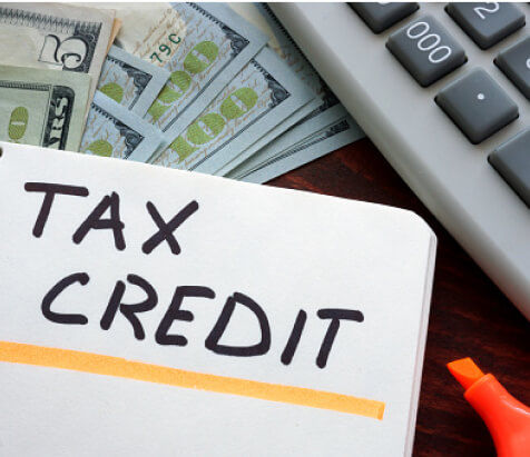 Money, computer and notepad with "Tax Credit" written on it