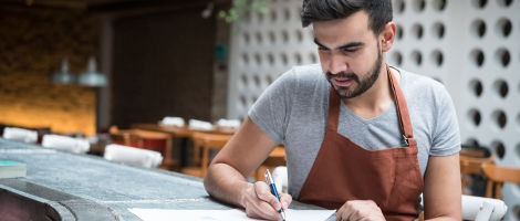 man wearing apron sitting at the counter of a restaurant working on his three year plan