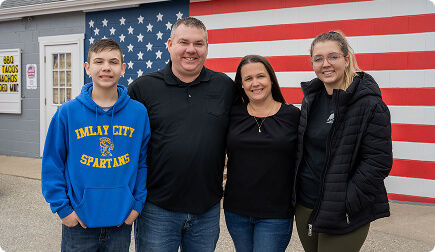 Couple with their two kids smiling at the camera in front of an American flag