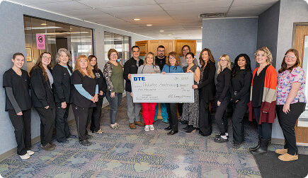 Group of people looking at the camera and holding a large DTE Energy Efficiency Contest check.