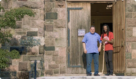 Two men in front of a church door smiling at the camera.