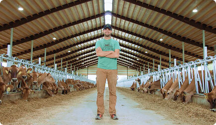 Man smiling at the camera in front of a cattle farm