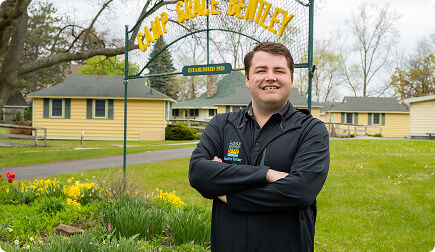 Man smiling at the camera with sign behind Camp Grace Bentley