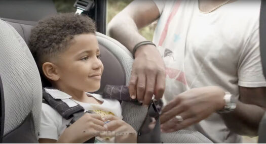 Young boy getting buckled in car seat by his dad