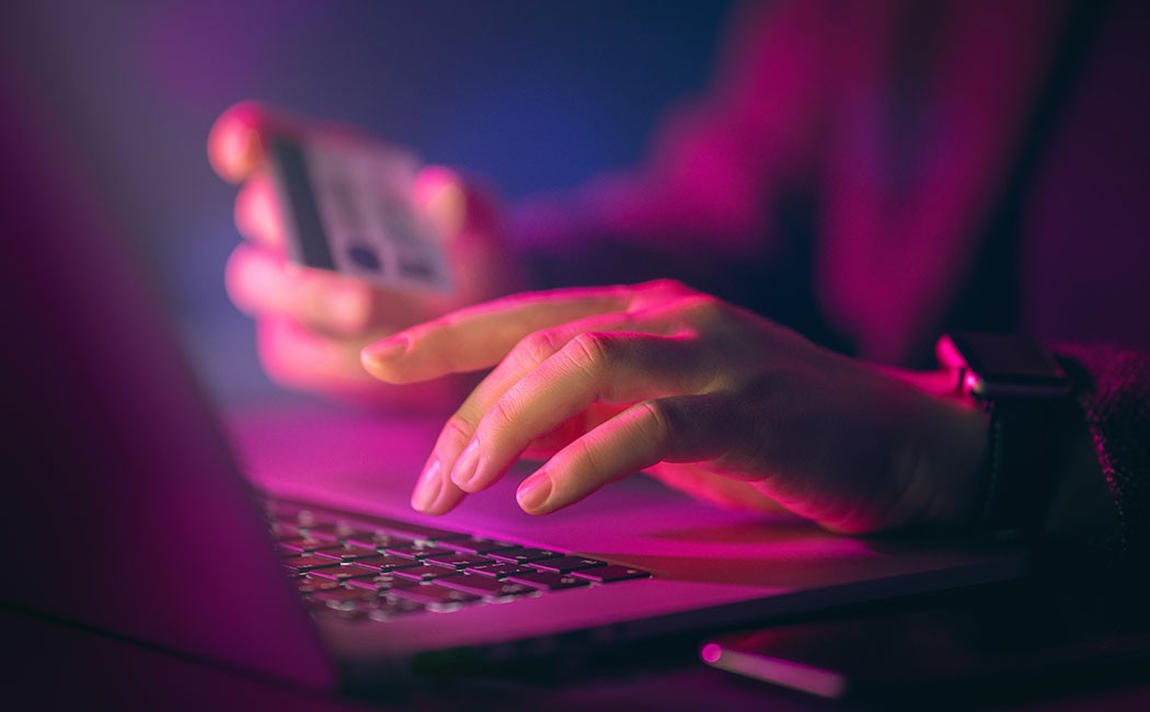 Woman typing on laptop holding credit card, FCM Bank, Banking BPS | DXC Technology customer story