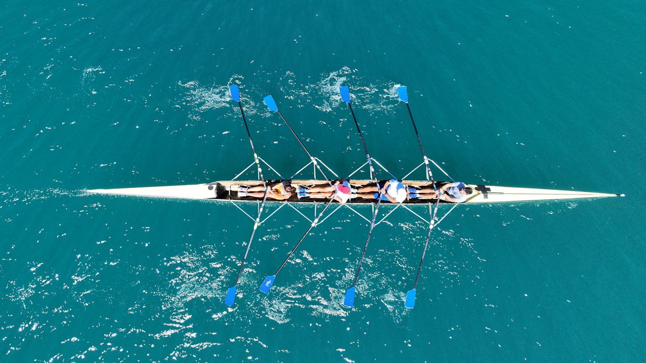 Aerial view of four rowers in a sport boat on emerald water | DXC Technology Campaign