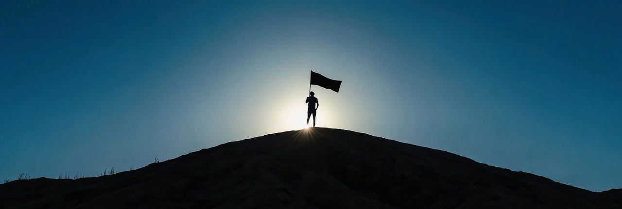 Person standing on hilltop holding flag as sun sets, Cloud Platforms | DXC Technology Private AI