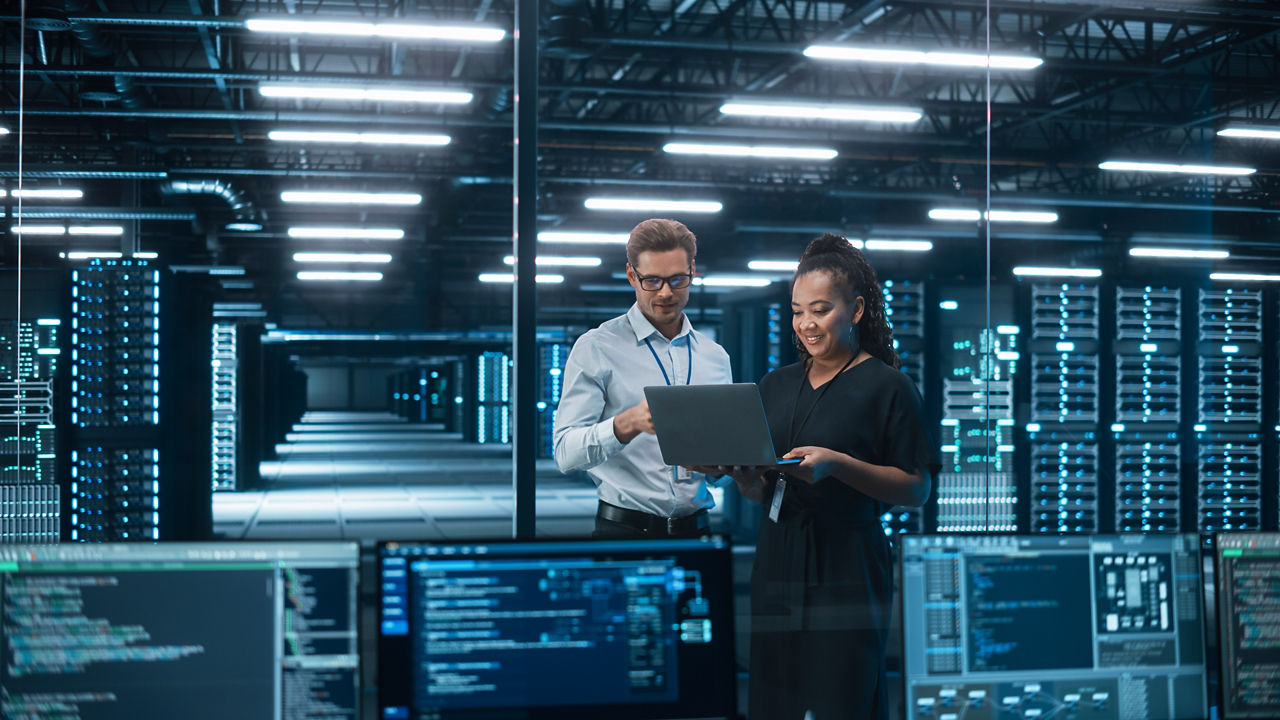 Two IT professionals in data center reviewing laptop data to streamline deployment and reduce disruptions, Zero trust solutions | DXC Technology