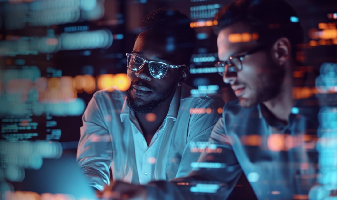 Two male software engineers reviewing code on a screen in a dark room