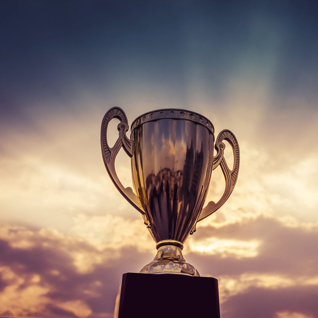 Silver trophy cup against rays of sun in cloudy sky, Everest Group Leader Award 2022 for ServiceNow services | DXC Technology