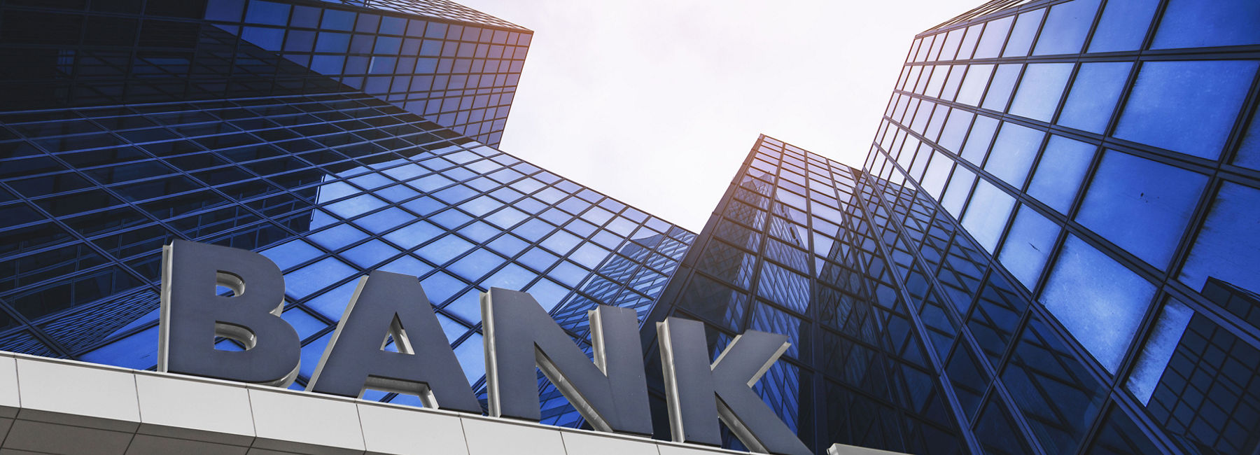 View from sidewalk towards bright sky, with office buildings on every side, DXC and Google Cloud in banking | DXC Technology