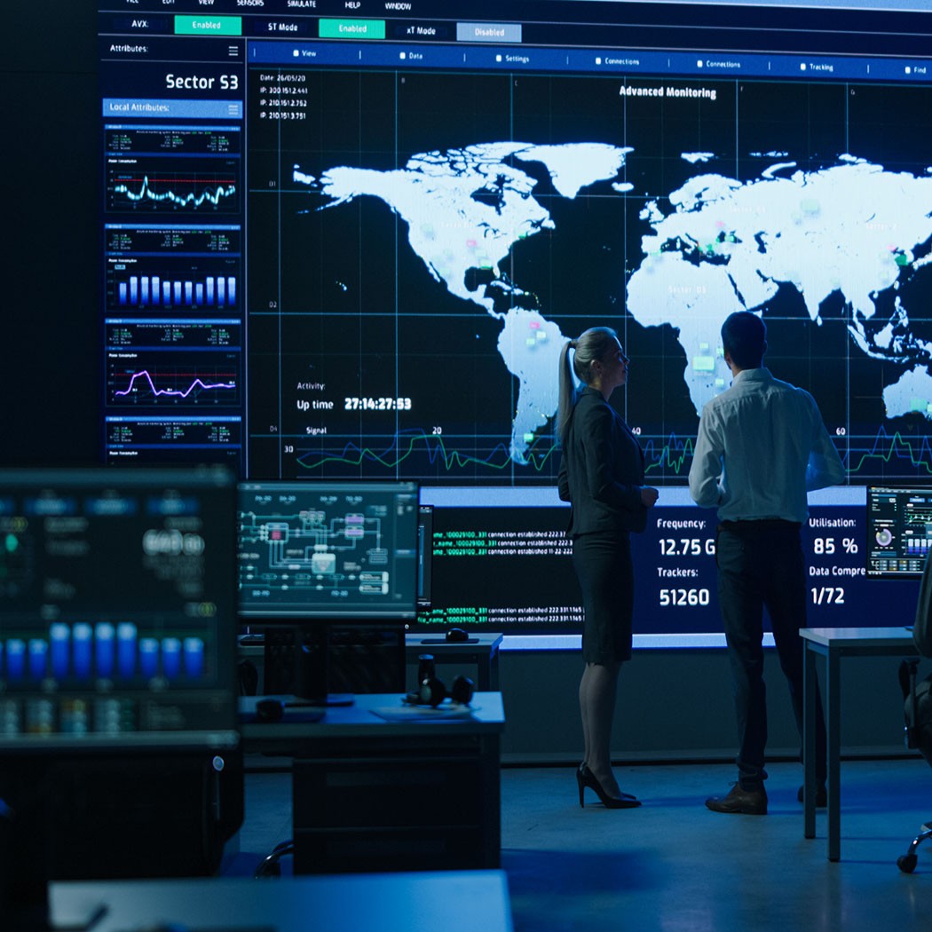 Project Manager Uses Digital Tablet Talks with Computer Scientist Looks at Big Screen Display Showing Infographics Global World Map Data. Telecommunications Control Control Room with People Working