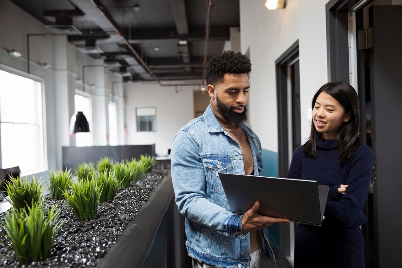 Smiling colleagues discussing over laptop computer while standing in office